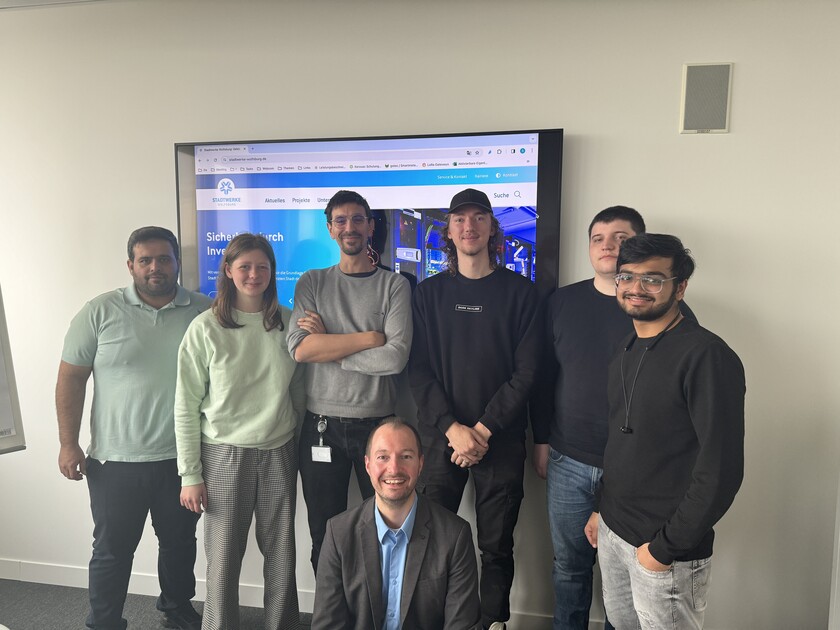 Personen stehen gemeinsam vor einem Bildschirm.