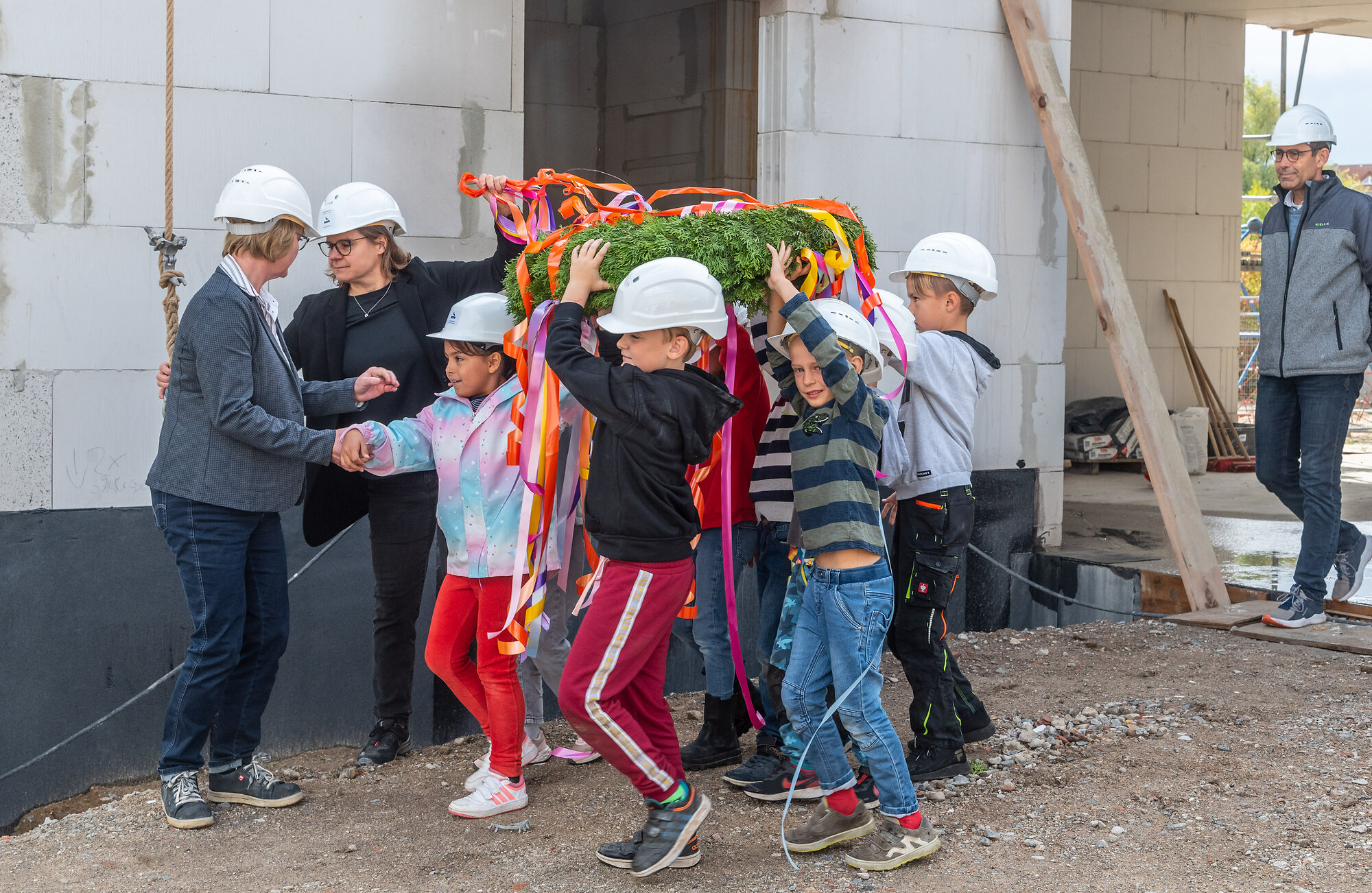 Kurz vor dem symbolischen Akt: Die Grundschüler:innen bringen den selbst gefertigten Richtkranz gemeinschaftlich zur Baustelle.