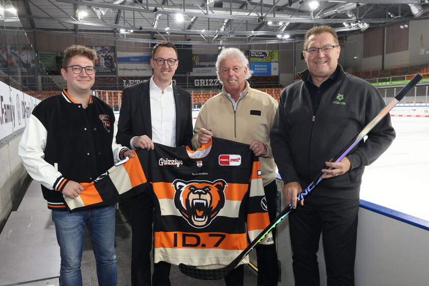 Leiter Organisation & Marketing bei den Grizzlys, WOBCOM-Geschäftsführer, Grizzly-Geschäftsführer und der WOBCOM-Abteilungsleiter stehen aufgereiht mit einem Eishockeyschläger und einem Grizzly-Trikot nebeneinander.