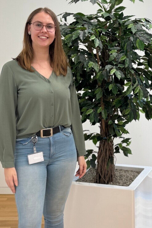 Nadine_Nachhaltigkeit Nadine Kreipe steht vor einer grünen Pflanze und lächelt in die Kamera