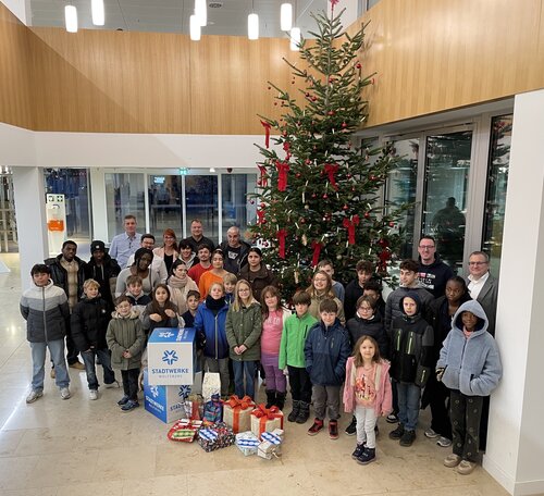 Die Kinder des Kinder- und Jugendschutz Wolfsburg e. V. des Tabaluga Kinderhaus stehen mit den Geschenken vor einem Weihnachtsbaum