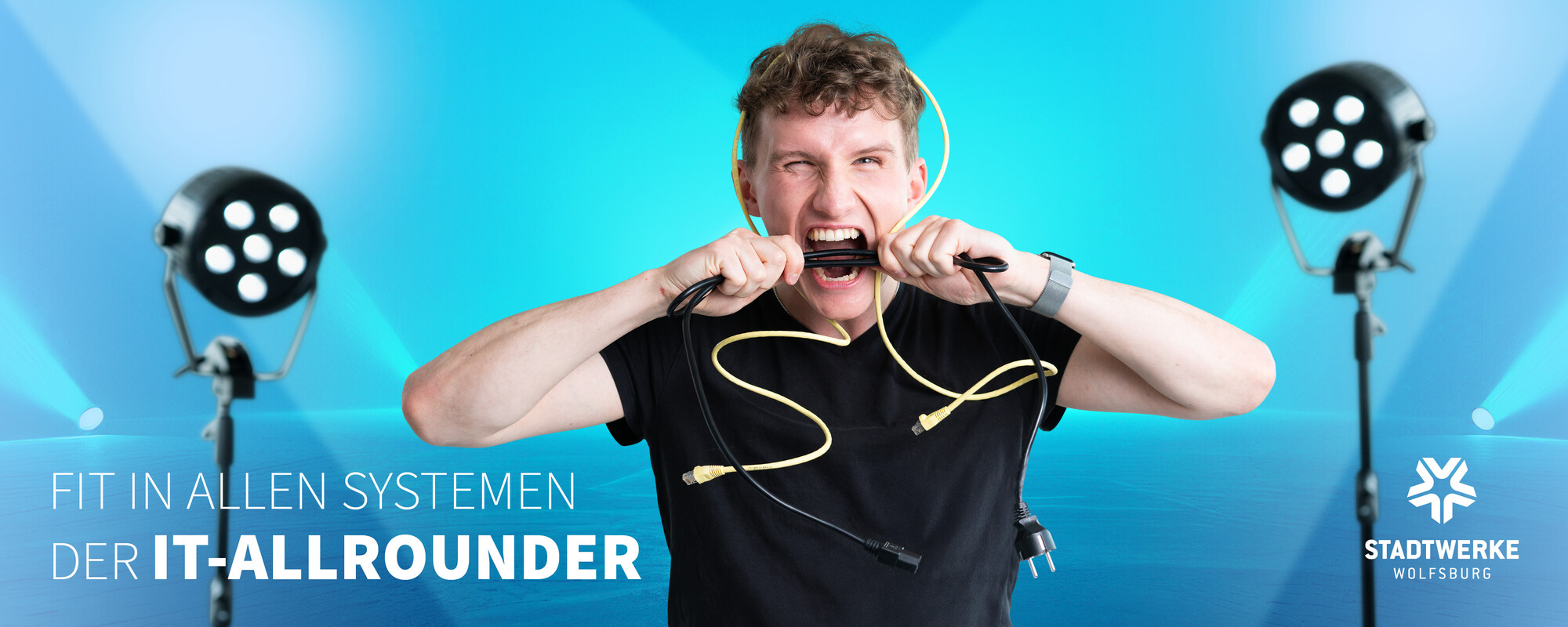 Ein junger Mann mit einem Netzwerkkabel über dne Kopf beisst in ein Stromkabel. Text: Fit in allen Systemen - Der IT-Allrounder