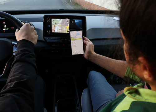 Beifahrer schaut in die WolfsburgApp, die eine freie Ladesäule an seinem Fahrtziel anzeigt.