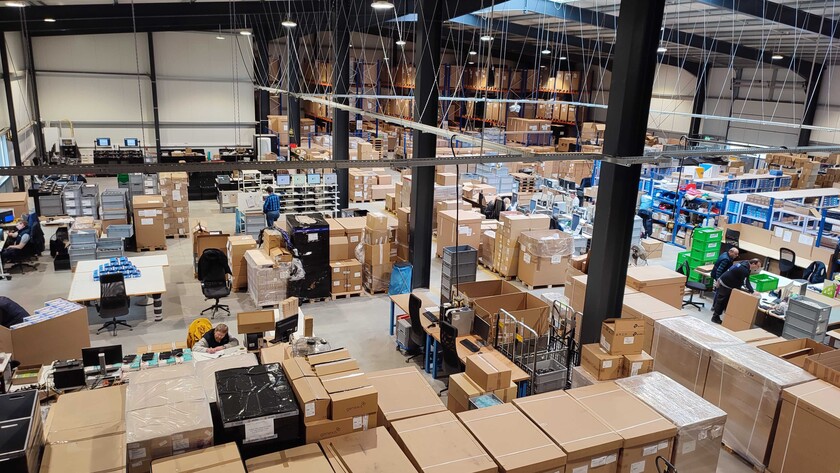 Green Router_Seloca_Überblick Einblick in die Arbeitsstätte von SELOCA. Man sieht Regale mit Kisten und Kartons, Schreibtische und Tische sowie Menschen, die arbeiten.