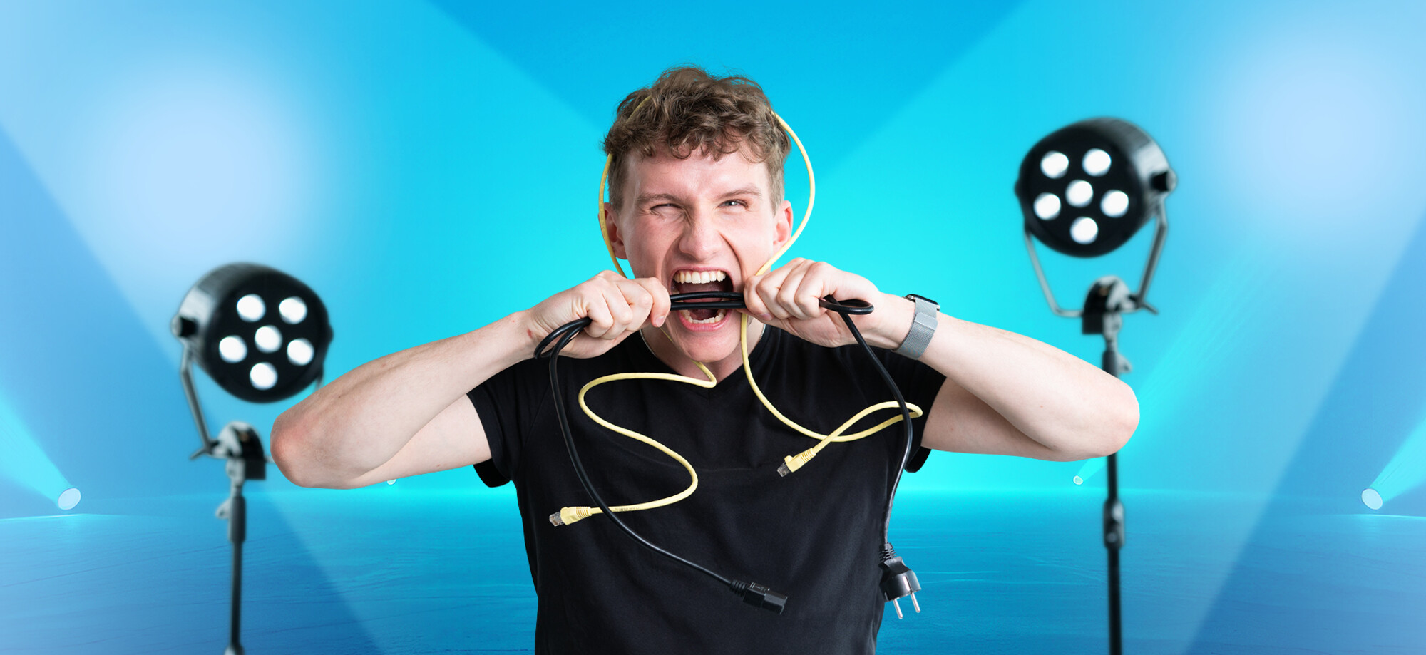 Ein junger Mann mit einem Netzwerkkabel über den Kopf beisst in ein Stromkabel.