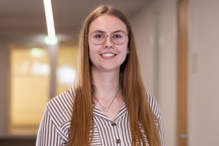 Nadine Kreipe, eine junge Frau mit langen, braunen Haaren und einer Brille lächelt in die Kamera. Sie trägt eine gestreifte Bluse.